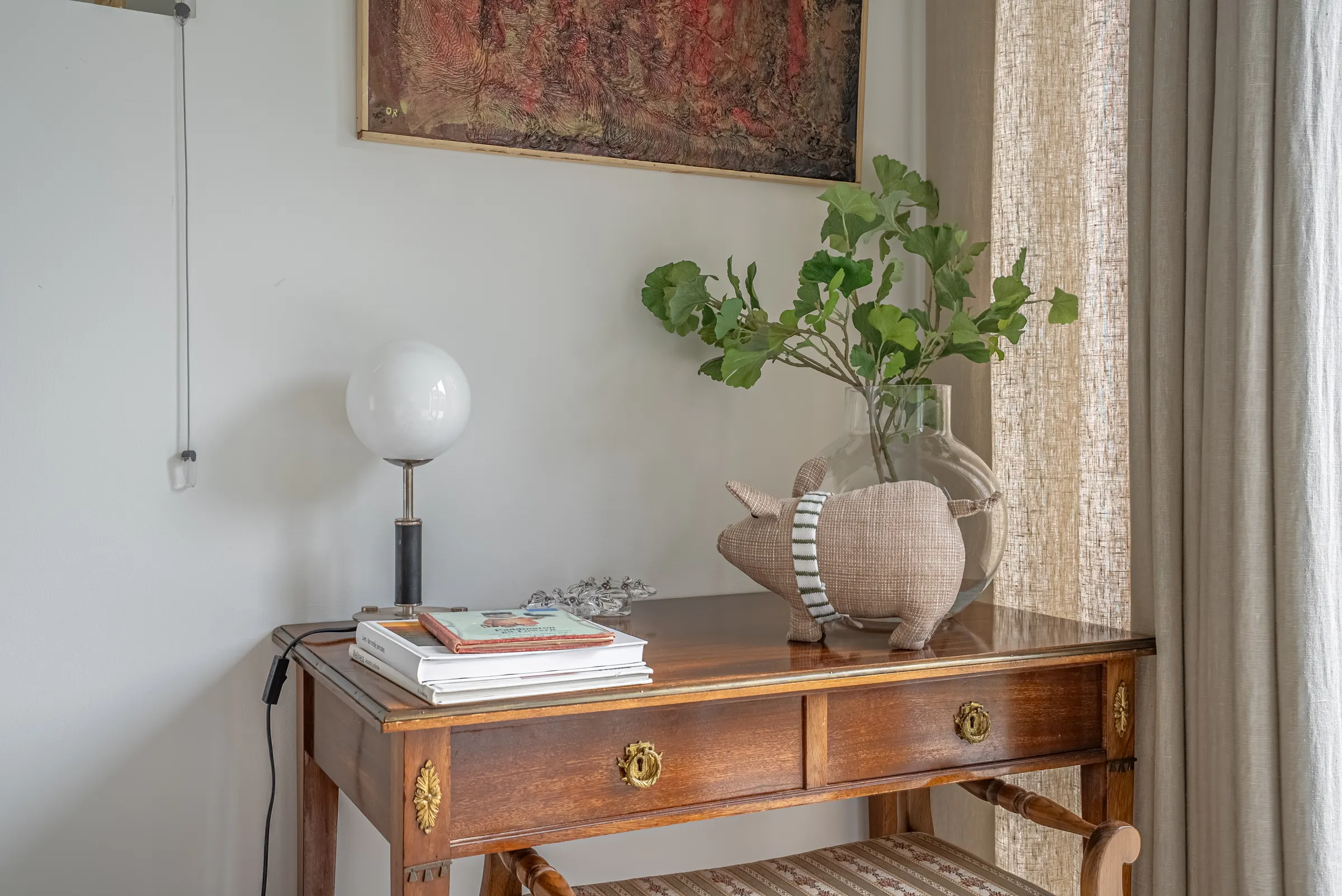 Detalj: byrå med lampa, böcker och en vas med grenar