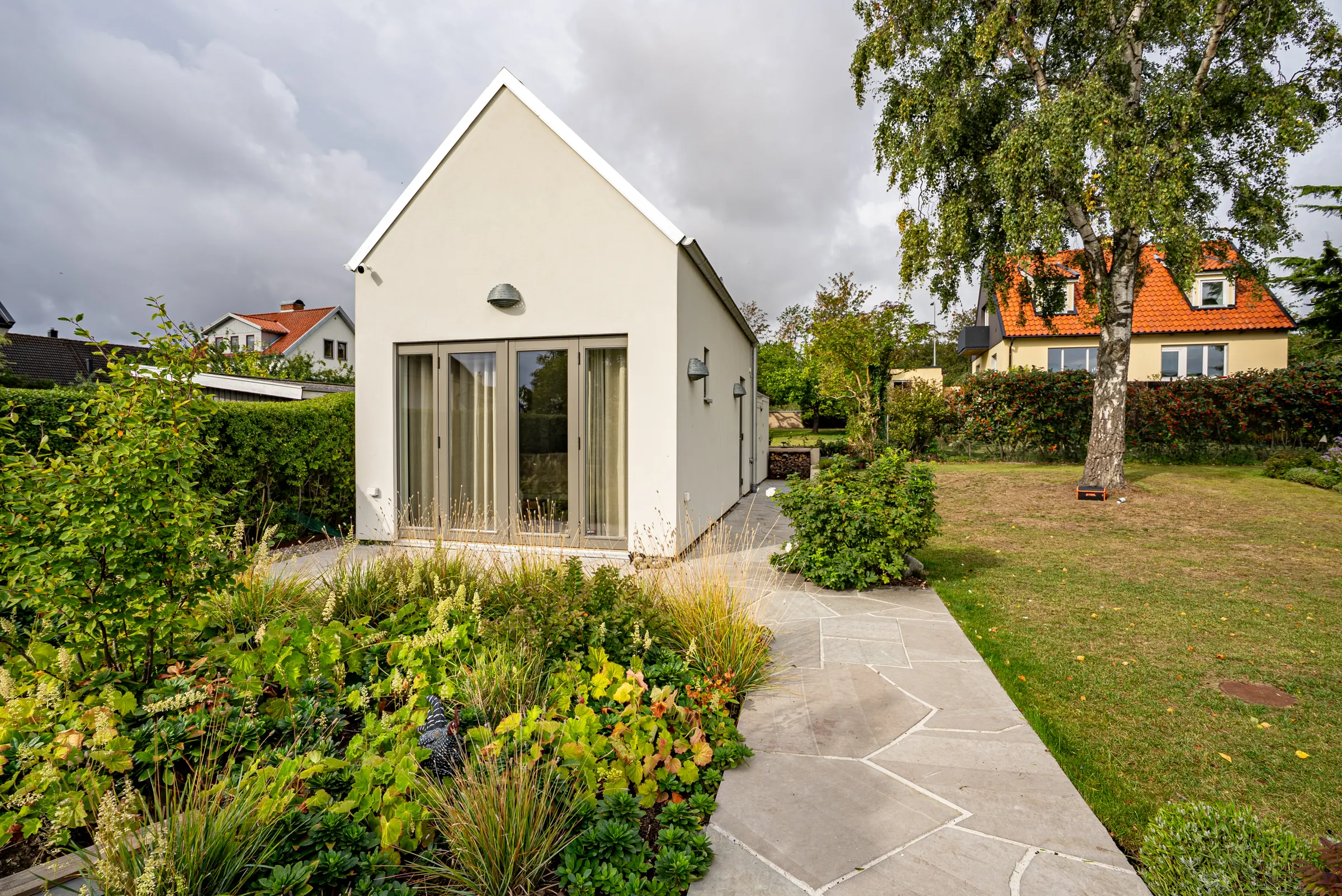 Gästhus med trädgård, stenlagd gång och gräsmatta