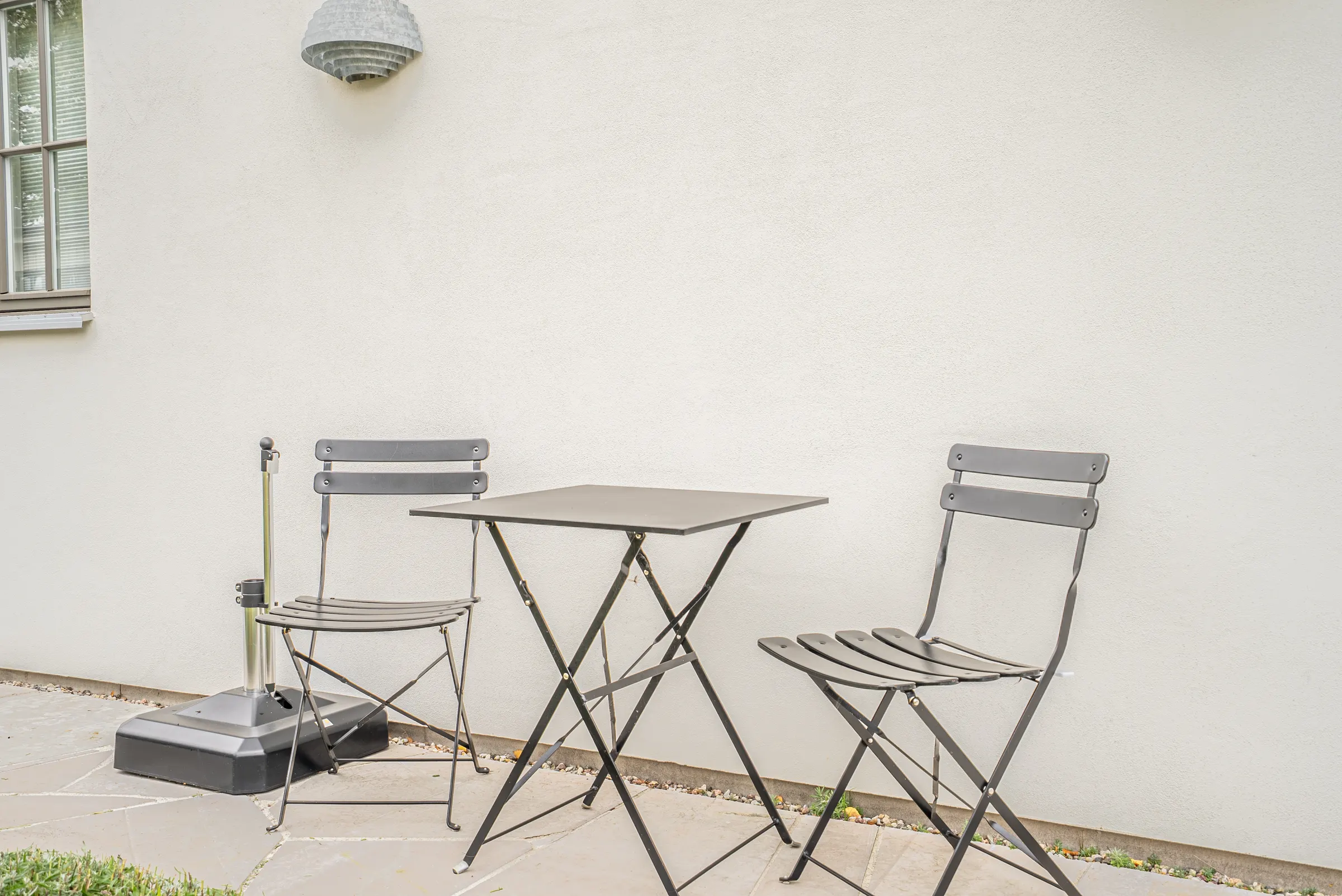 Uteplats med bord och stolar mot en vit vägg